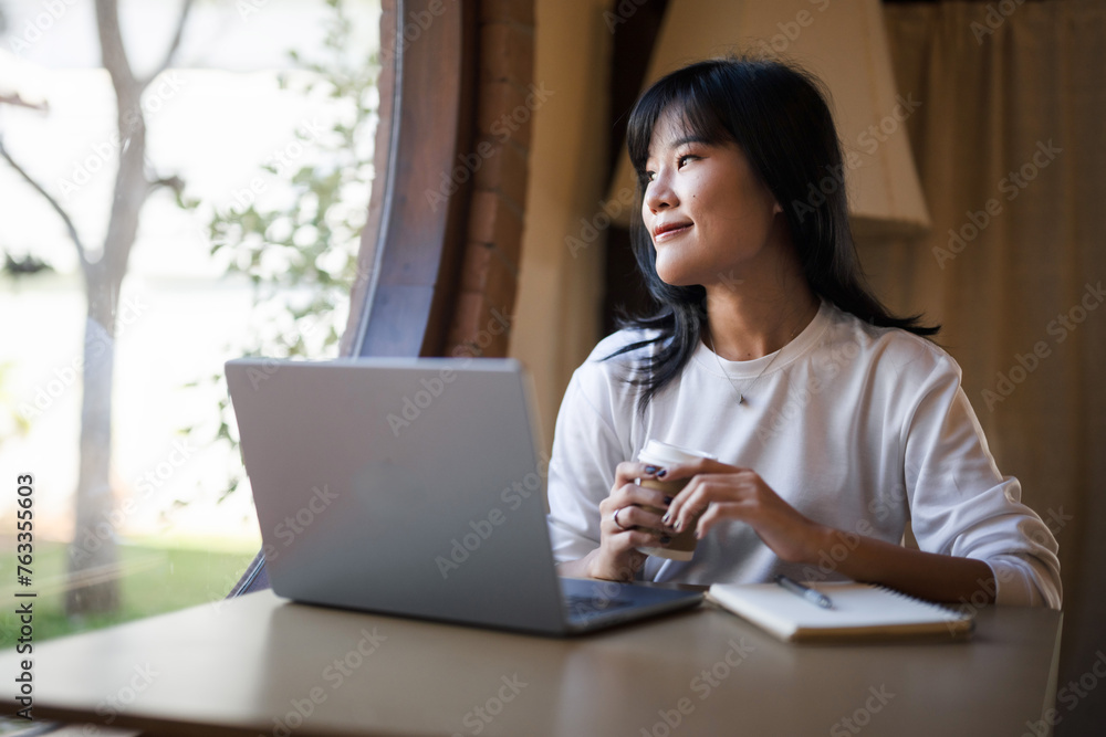 Young Asian woman taking a coffee break while working remotely in a coffee shop. Young Asian woman taking a coffee break while working remotely in a coffee shop.