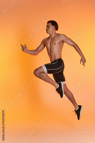 appealing shirtless man in black shorts exercising actively and looking away on orange backdrop