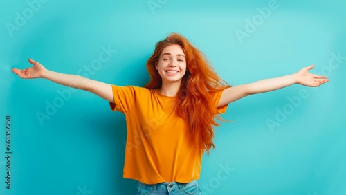 A woman in an orange shirt opens her arms in preparation for a hug on a blue background. © PJang