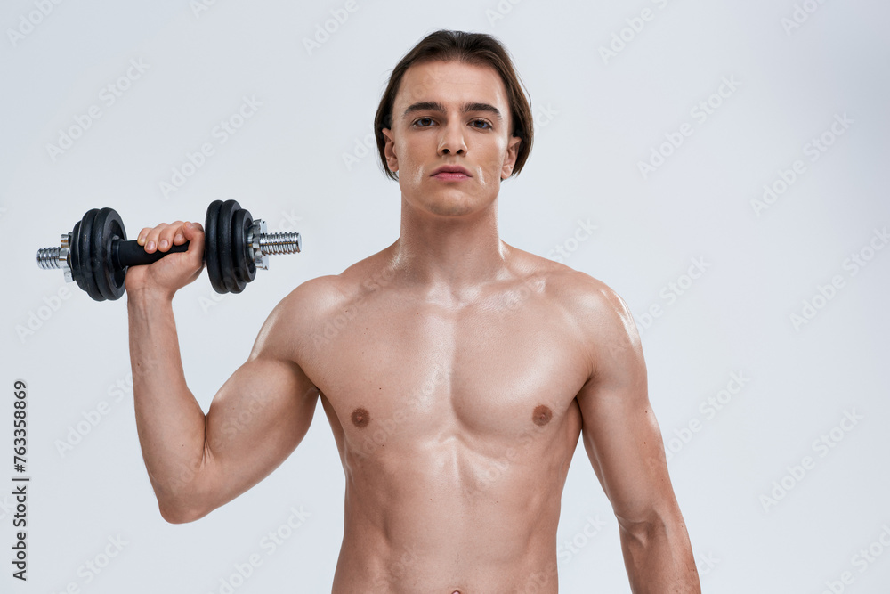 good looking athletic man posing topless exercising actively with dumbbell and looking at camera good looking athletic man posing topless exercising actively with dumbbell and looking at camera
