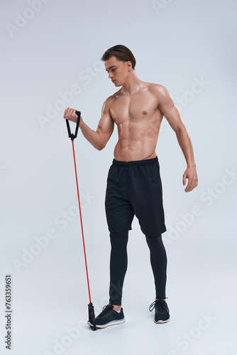 alluring shirtless sporty young man in black pants training with fitness expander and looking away