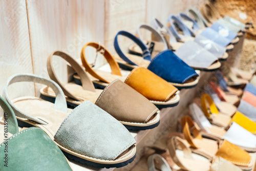 A shelf displays a variety of handmade leather sandals in various pastel colors, which show the Menorcan craftsmanship and traditional summer footwear style of the island. photo