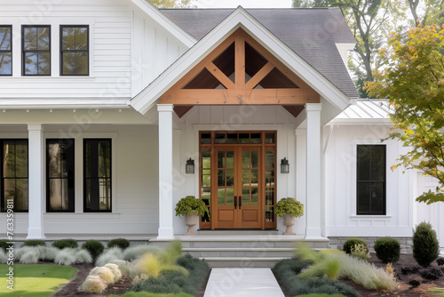 A front door detail of a white modern farmhouse with a wooden front door, black light fixtures, white oak accents, and a covered porch.