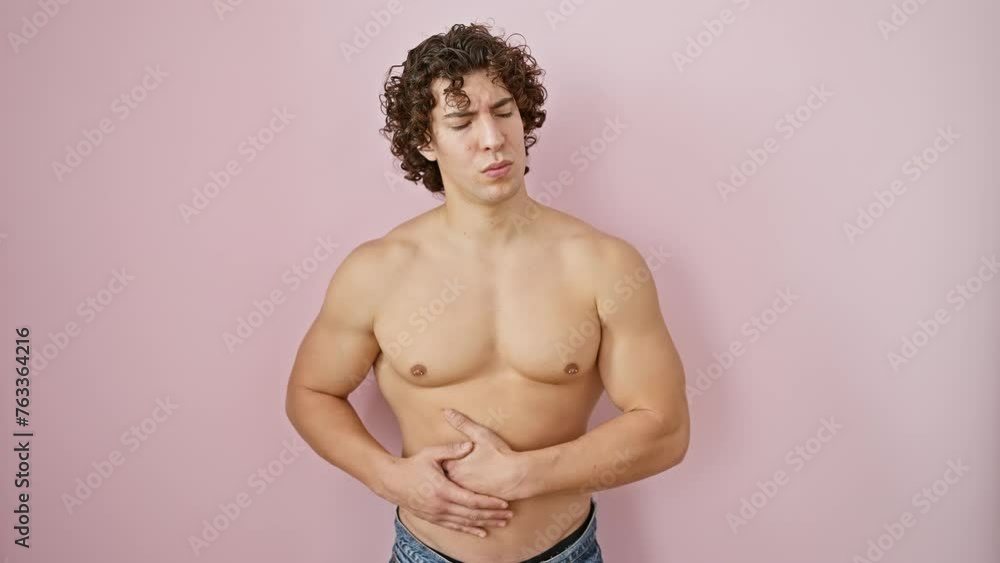 Troubled young hispanic man, shirtless, gripping his stomach in pain, experiencing nausea from a possible medical illness, isolated over pink background Troubled young hispanic man, shirtless, gripping his stomach in pain, experiencing nausea from a possible medical illness, isolated over pink background