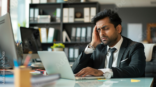 Exhausted indian businessman feeling stressed at work while sitting at his office desk