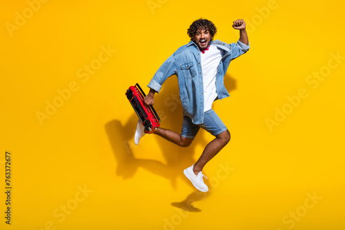 Full body photo of attractive young man raise fast excited boombox wear trendy denim clothes red scarf isolated on yellow color background