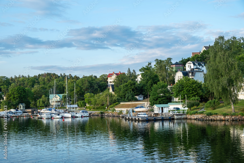 Fototapeta premium Archipelago, Stockholm Sweden. Seafront villa, yacht, reflection in ripple water, cloudy sky.