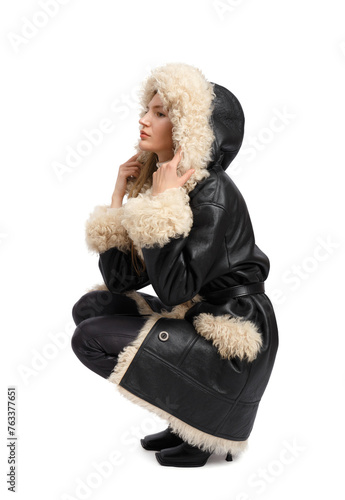 A girl in a sheepskin coat sits on a white background