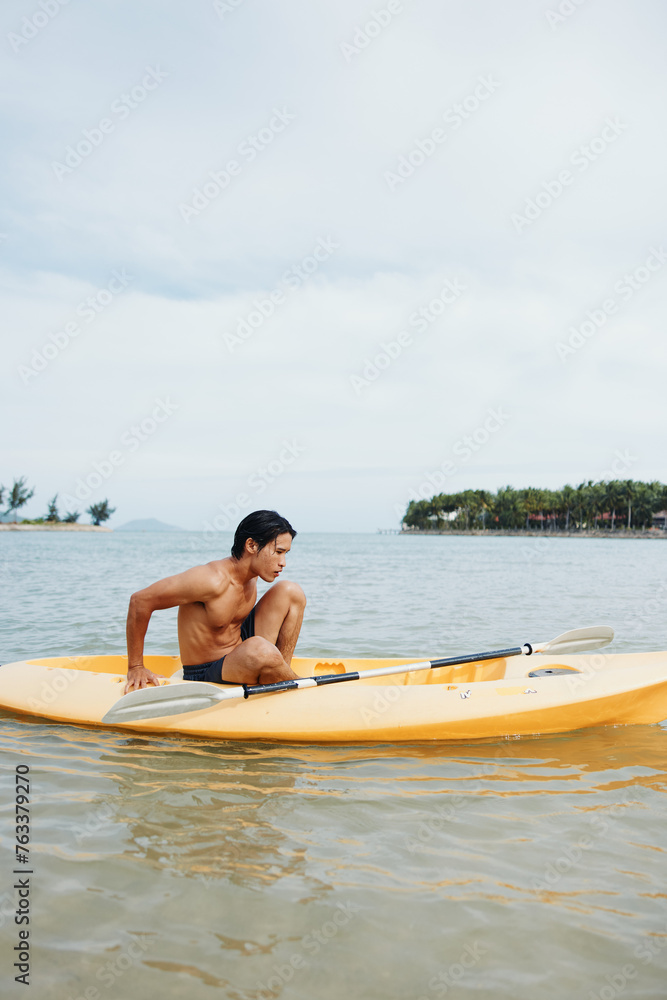 Happy Asian Man Kayaking on a Tropical Beach: Enjoying Leisure and Adventure on the Sunlit Water.