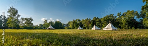 An outdoor meadow with white camping tents against a background of blue sky and green trees.