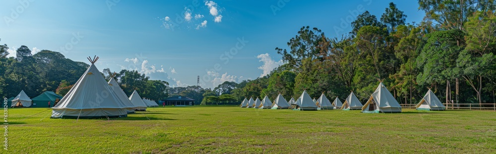 An outdoor meadow with white camping tents against a background of blue sky and green trees.