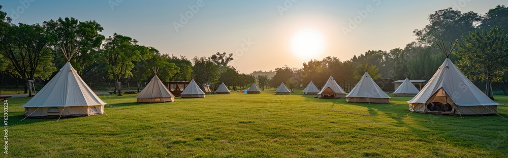 An outdoor meadow with white camping tents against a background of blue sky and green trees. An outdoor meadow with white camping tents against a background of blue sky and green trees.