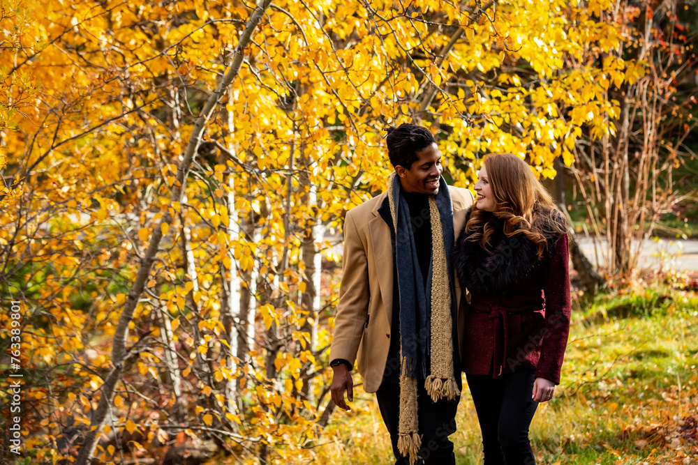A mixed race couple walking through the woods smiling at each other while spending quality time together during a fall family outing in a city park; Edmonton, Alberta, Canada A mixed race couple walking through the woods smiling at each other while spending quality time together during a fall family outing in a city park; Edmonton, Alberta, Canada