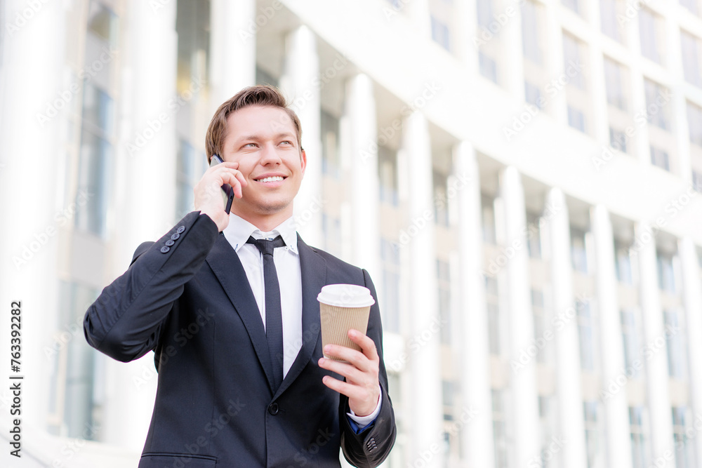 Fototapeta premium Good talk. Cheerful young business man talking on the mobile phone and holding cup of coffee.