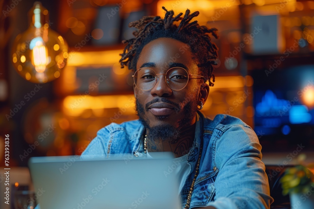 Obraz premium Smiling man with glasses in a cozy illuminated workspace.