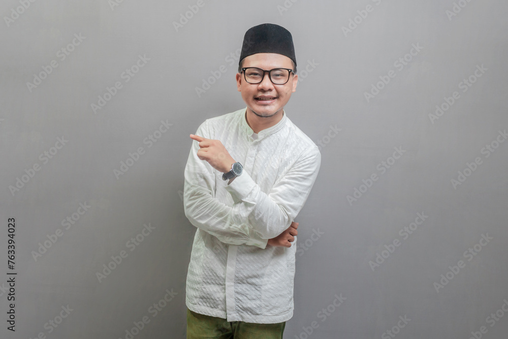Asian Muslim man standing looking camera and pointing finger to right empty space Asian Muslim man standing looking camera and pointing finger to right empty space