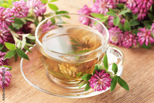 Red clover tea or extract in glass cup with leaves and flowers on wooden background, closeup, remedy for menopause, source of estrogen, used in cosmetics, spa, face and hair beauty