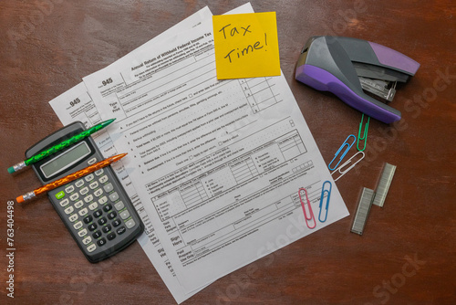 Flat lay of tax form 945 for federal taxes for self employment and freelance work with calculator and reminder note on wood background and copy space