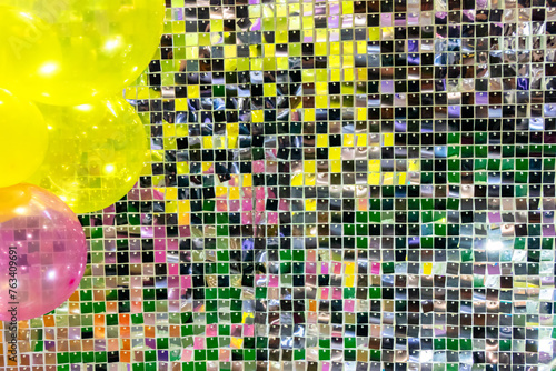 A mosaic background of silver glitter tiles with a yellow balloon behind it. The tiles add a playful and festive atmosphere to the scene.