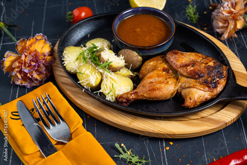 Half of a roasted chicken, on a black plate with herbs and tomatoes, on a dark concrete photo