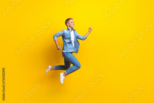 Full length photo of lovely young lady running fast shopping wear trendy jeans garment isolated on yellow color background