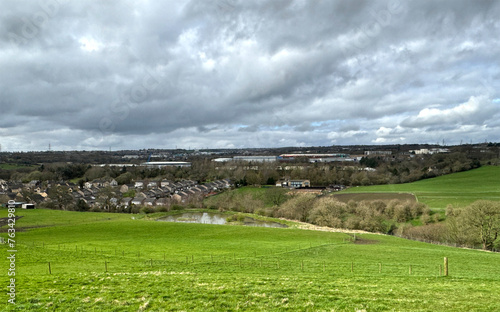 Landscape view from, Cliff Hollins Lane, with a large field, a lake, and distant houses, on a cloudy day near, Dewsbury, UK photo