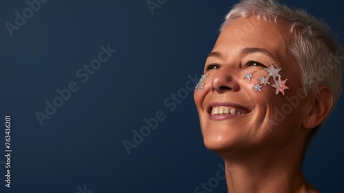 A content senior woman, gazing upward with a warm smile and festive starry face decoration, set against a deep blue background. photo