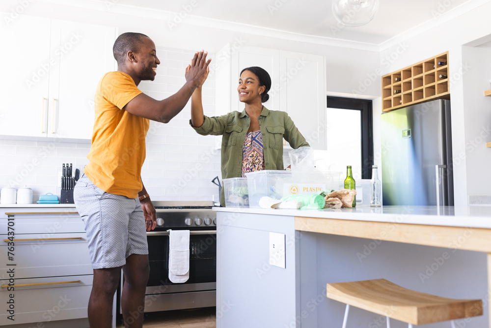 A diverse couple recycling together in a kitchen with a high-five at home A diverse couple recycling together in a kitchen with a high-five at home