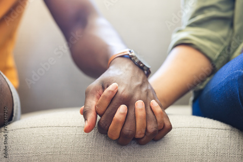 A diverse couple holds hands on the couch, showing unity and affection photo