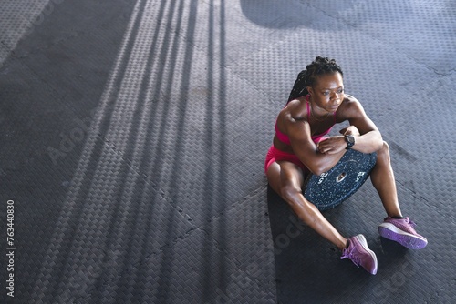 A fit African American strong woman sits on a black mat in the gym with copy space photo