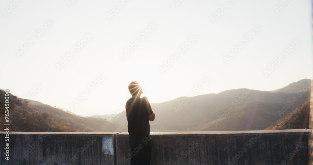 A man stands on a ledge looking out over a mountain range
