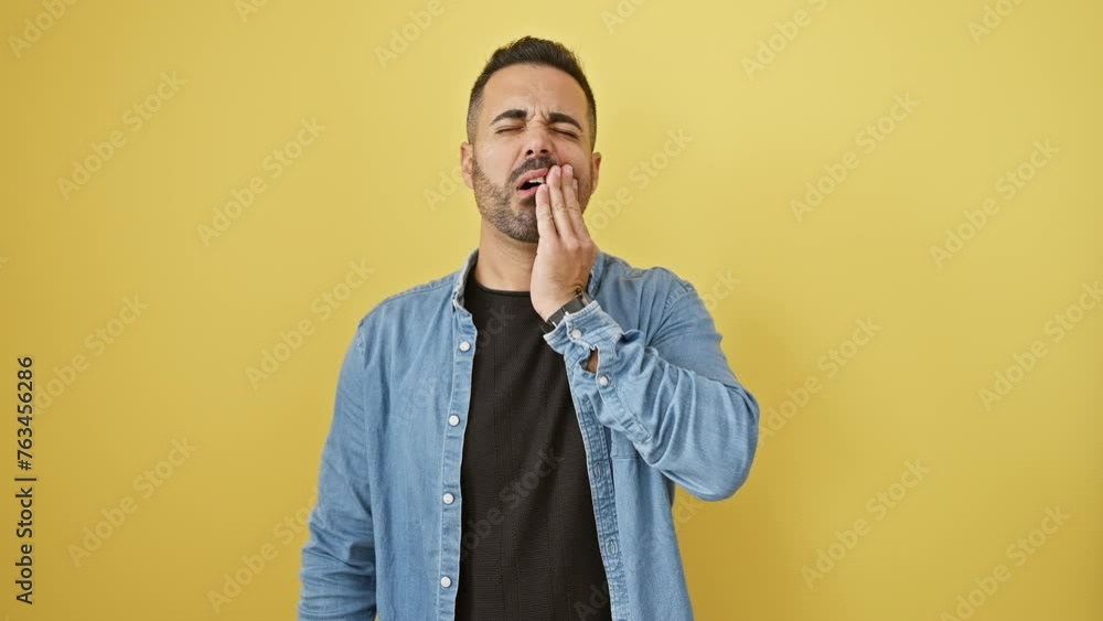 Hispanic guy in denim shirt wincing in dental pain, standing over yellow background Hispanic guy in denim shirt wincing in dental pain, standing over yellow background