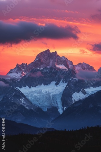 A mountain range stands in silhouette against a vivid sunset sky, creating a striking contrast between the dark peaks and the colorful sky