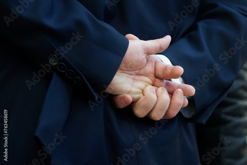 An adult man in a business suit holds his hands behind his back. Sign language. Photo.