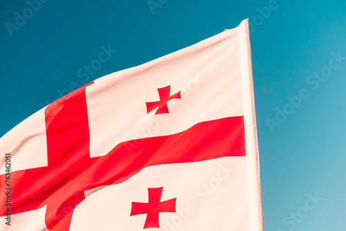 Fotografie The flag of Georgia flutters in the wind against the blue sky
