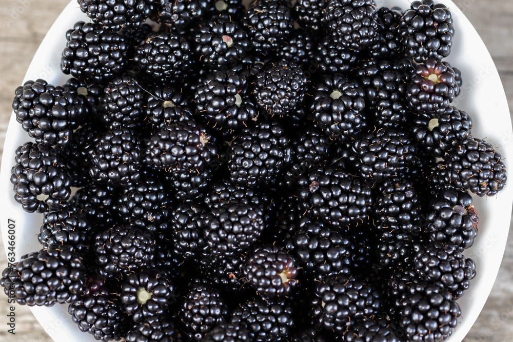 ripe black blackberries in a white plate on a wooden background . View from above. Copy space.Berry background ripe black blackberries in a white plate on a wooden background . View from above. Copy space.Berry background