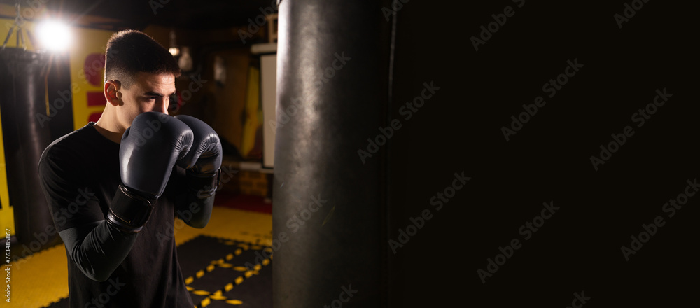 Young sportsman training boxing in the punching bag. Sport, self defense, boxing and training concept. Banner.