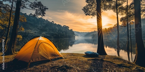 Yellow camp tent in front of beautiful lake in the forest with sun going up photo