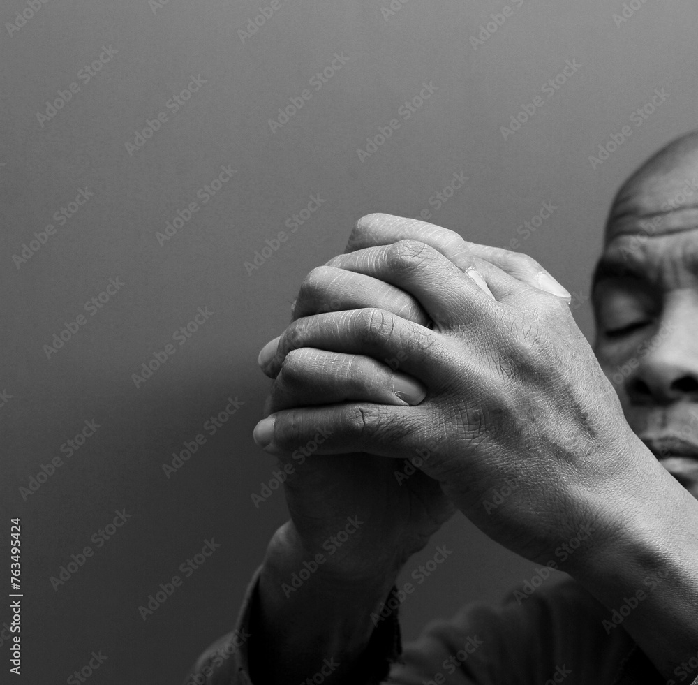 man praying to god with hands together Caribbean man praying with grey black background stock photo	