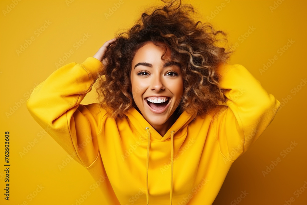 Portrait of a smiling young woman over yellow background. Young woman cute face expression posing in yellow hoodie on yellow background.