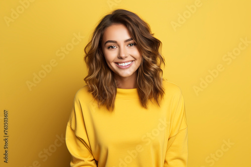 Portrait of a smiling young woman over yellow background. Young woman cute face expression posing in yellow hoodie on yellow background.