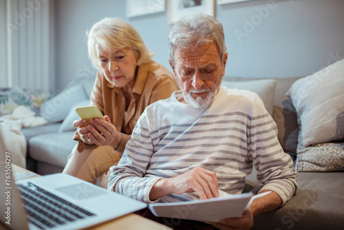 Senior couple reviewing documents and using smartphone on couch at home photo