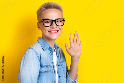 Photo portrait of pretty young girl specs wave palm hello wear trendy jeans outfit isolated on yellow color background