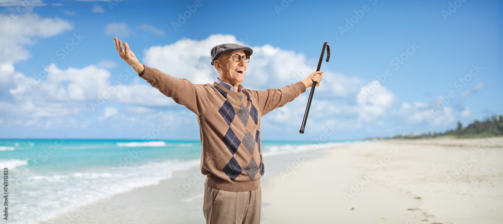 Elderly man with a cane spreading arms on a sandy beach - obrazy, fototapety, plakaty 