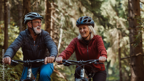 A retired couple wearing bike helmets are riding their electric bikes through a forest filled with tall trees and autumn foliage. 