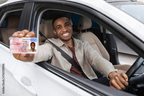  Happy young african man showing his driver's license from open car window