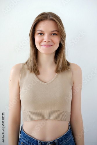 Young smiling beautiful girl model dressed in a beige top with a bare belly and blue jeans snap front look portrait view on white background