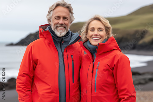 Portrait of a happy elderly couple with gray hair wearing red jackets on a day of hiking with backpacks