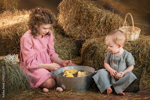 Two young children are sitting in a hay bale, one of them holding a basket.
