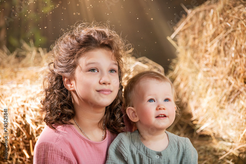 A young girl and a young boy are sitting together in a field of hay.
